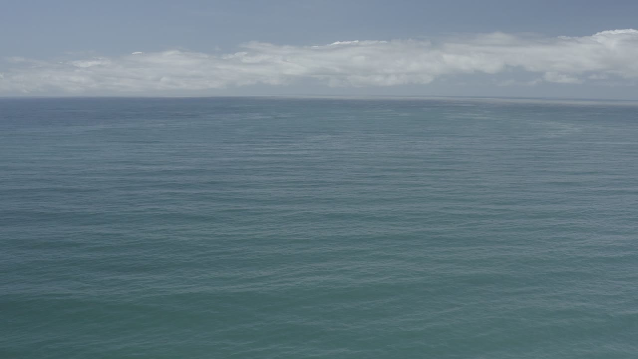 Wide view of blue-green ocean and pale sky in Los Cabos, Mexico, with a high straight horizon, low cloud band, and no visible people.