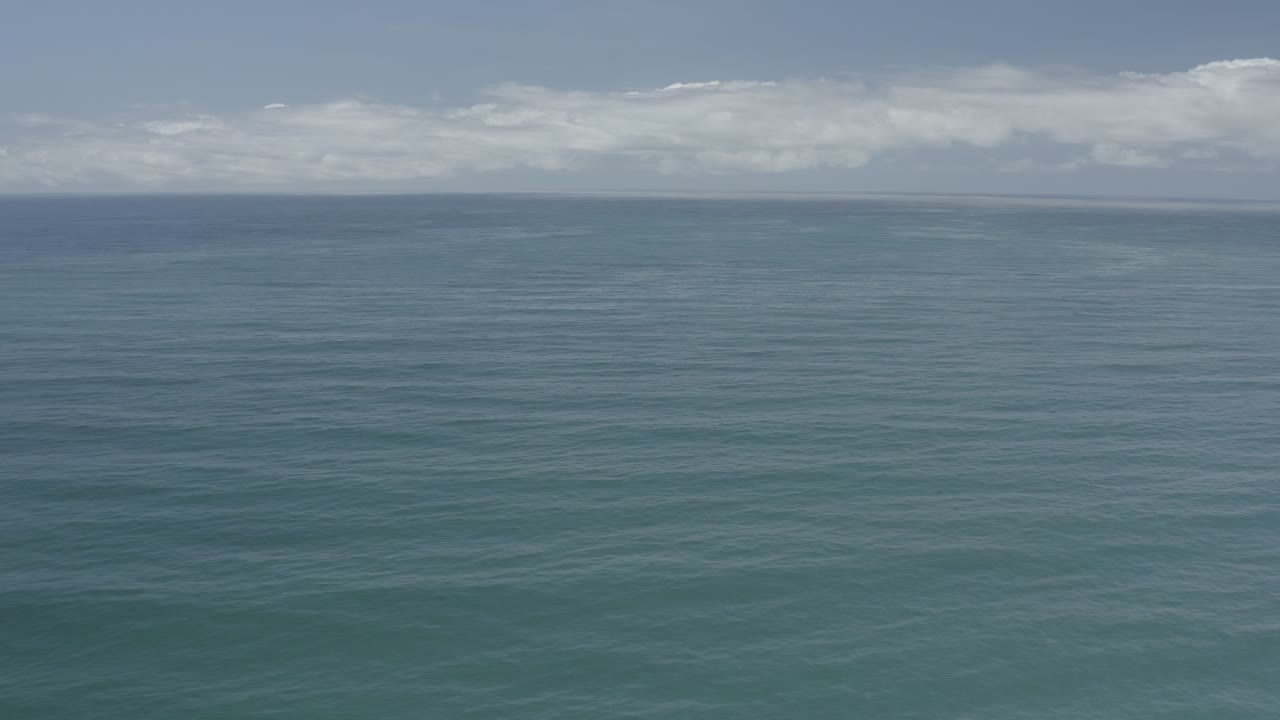 Open Los Cabos ocean view with rippled water in the foreground, a narrow horizon line, pale sky, low clouds, and no visible people.