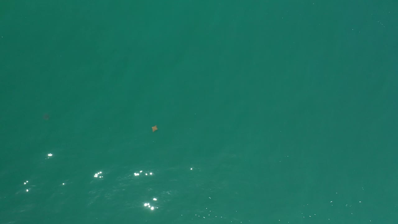 Clear teal ocean surface in Los Cabos with a faint darker underwater shape near the lower area and no visible people.
