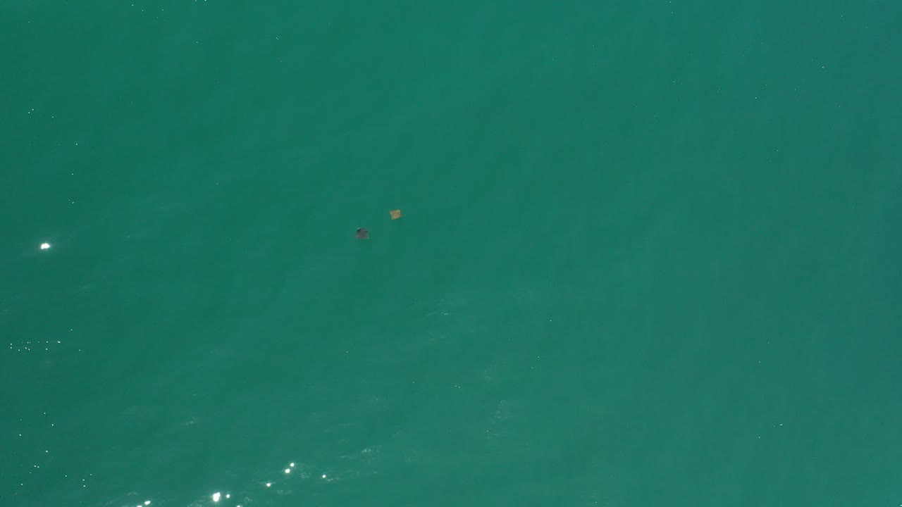 Opening frame of teal-green ocean water in Los Cabos, Mexico, with faint surface ripples, a few tiny floating specks, and no visible people.