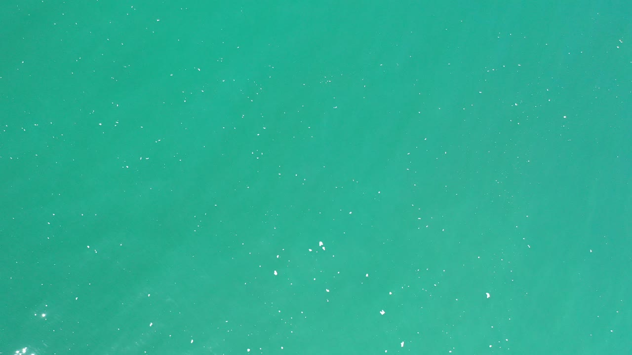 Turquoise-green ocean surface with small white sun glints.
