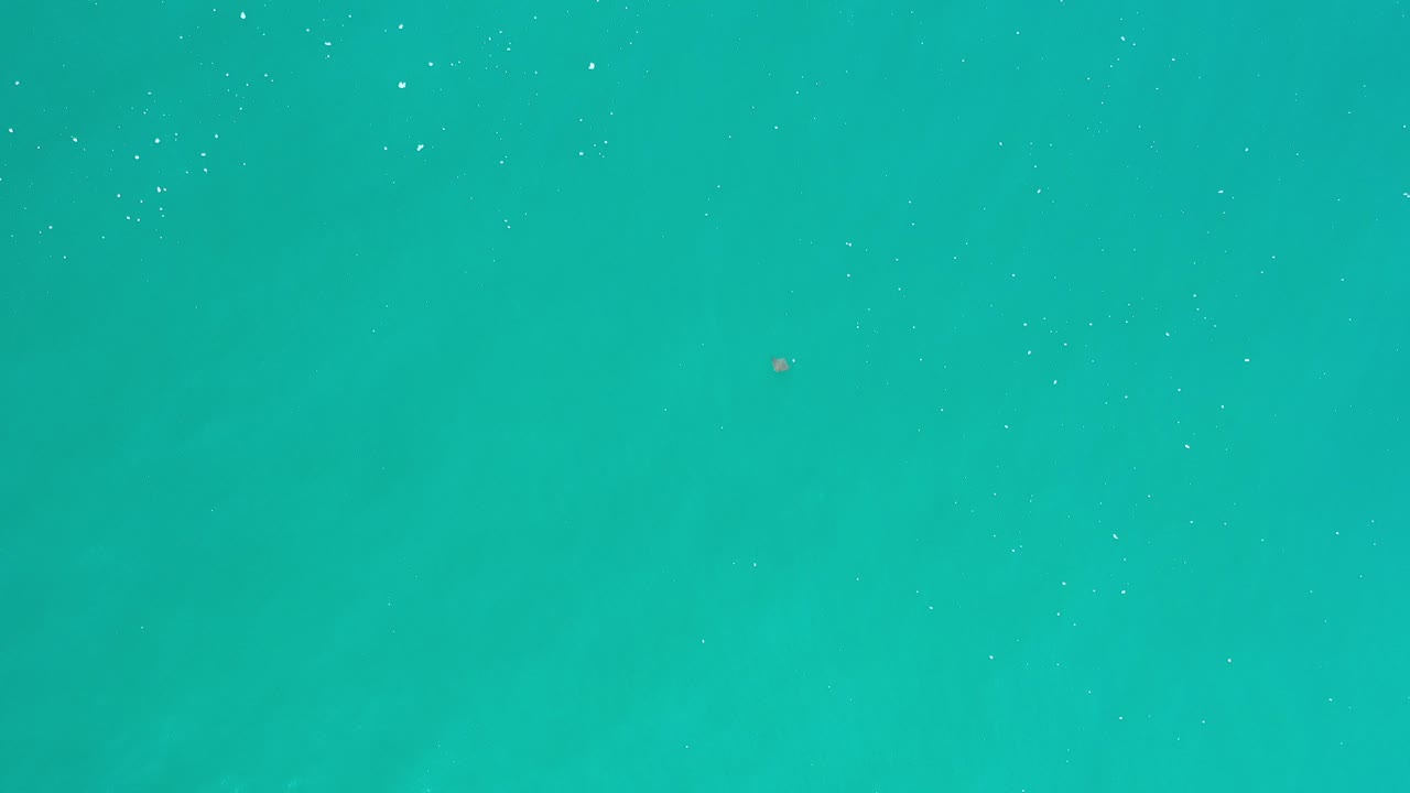Teal ocean water in Los Cabos fills the opening frame with scattered tiny bubbles, faint surface texture, and no visible people.