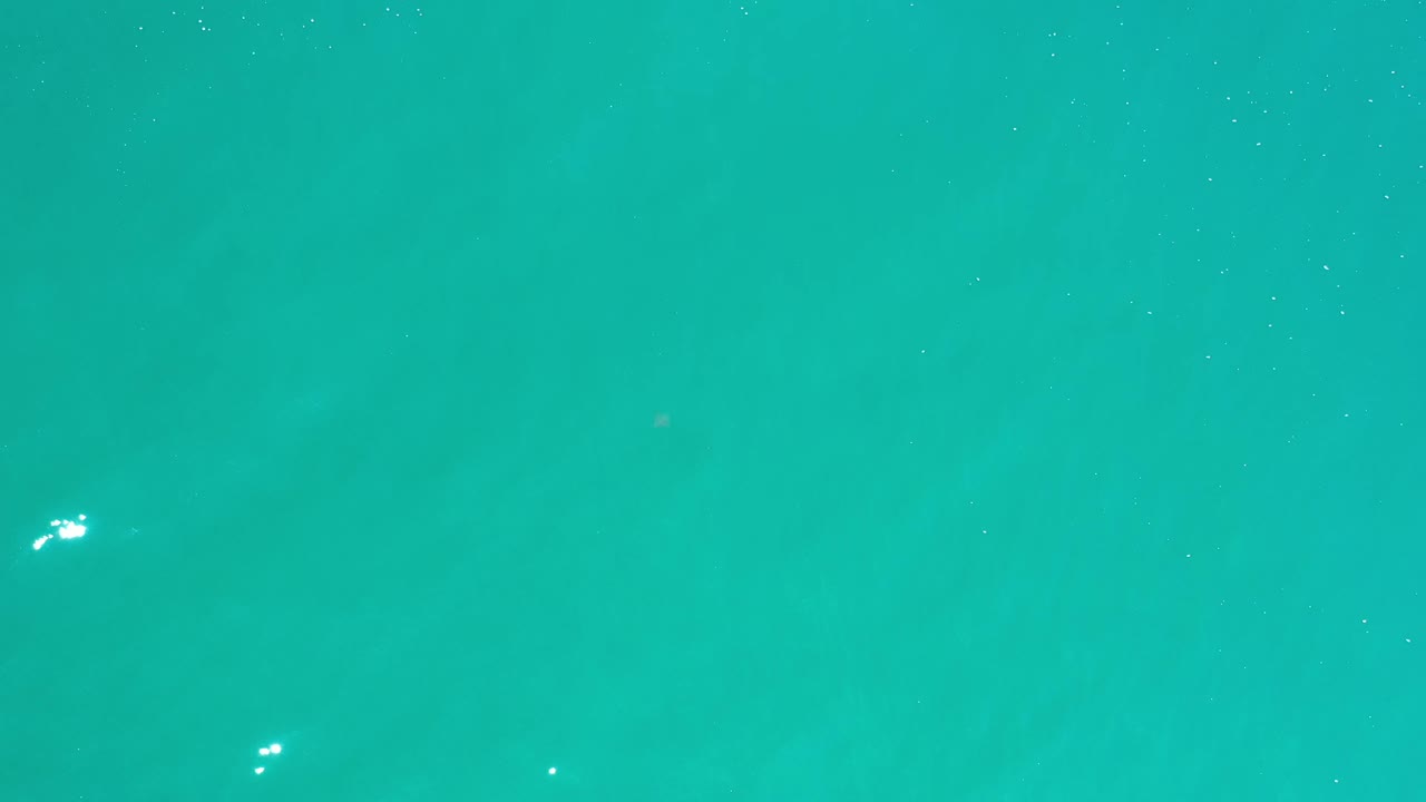 Overhead Los Cabos ocean frame with teal water, small white reflections near the center, and no visible people or shoreline.