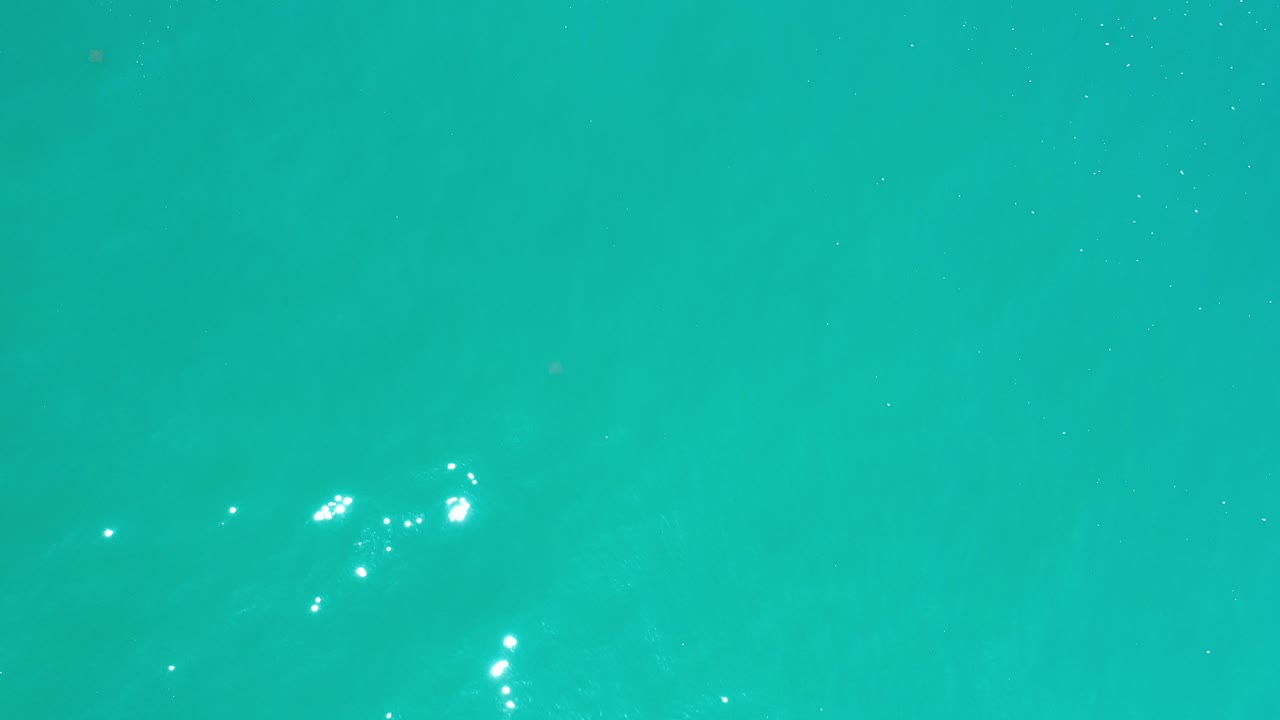 Overhead turquoise ocean water in Los Cabos, Mexico, with scattered bright sun glints near the lower left and no visible people.