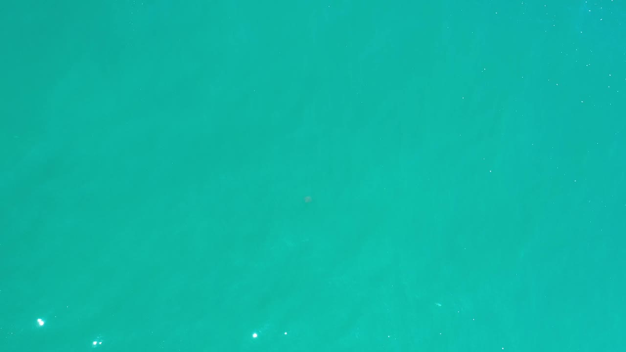 Bright teal water covers the full Los Cabos frame, with scattered sparkle near the upper right and no visible people.