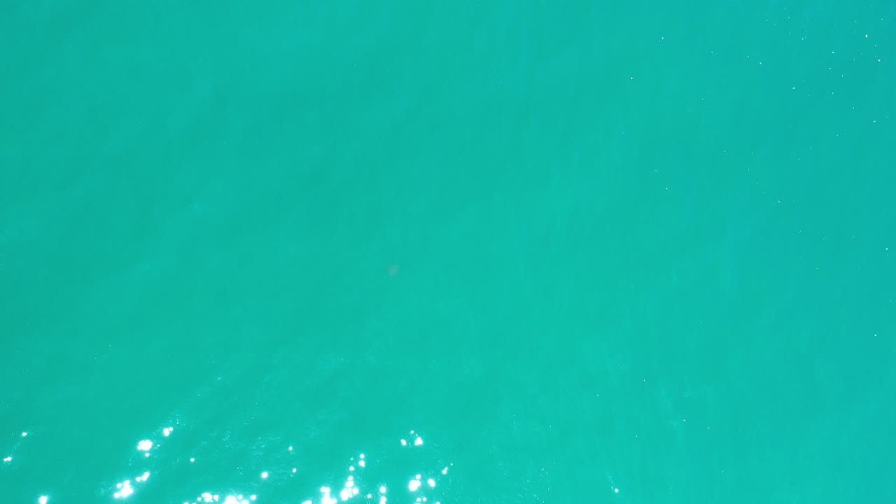 Bright turquoise water fills the first frame from Los Cabos, Mexico, with faint ripples and small white reflections, no visible people.