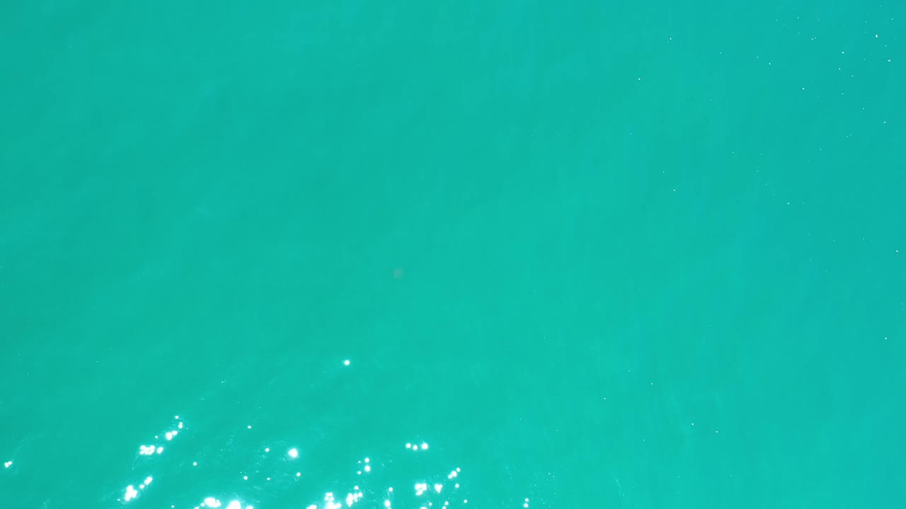 Aqua water in Los Cabos, Mexico, shows a slightly brighter cluster of sun glints near the lower part of the frame, with no visible people.
