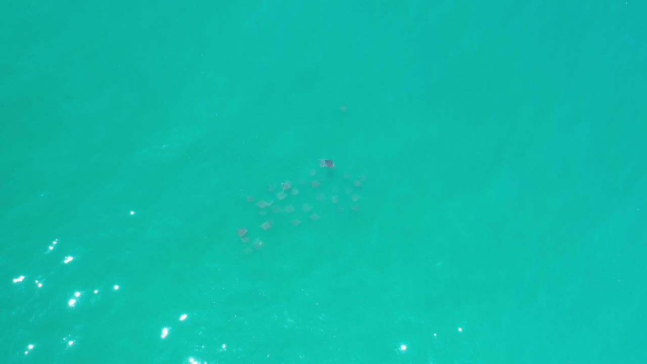 Turquoise sea surface with faint dark patches and sun glints to the right.