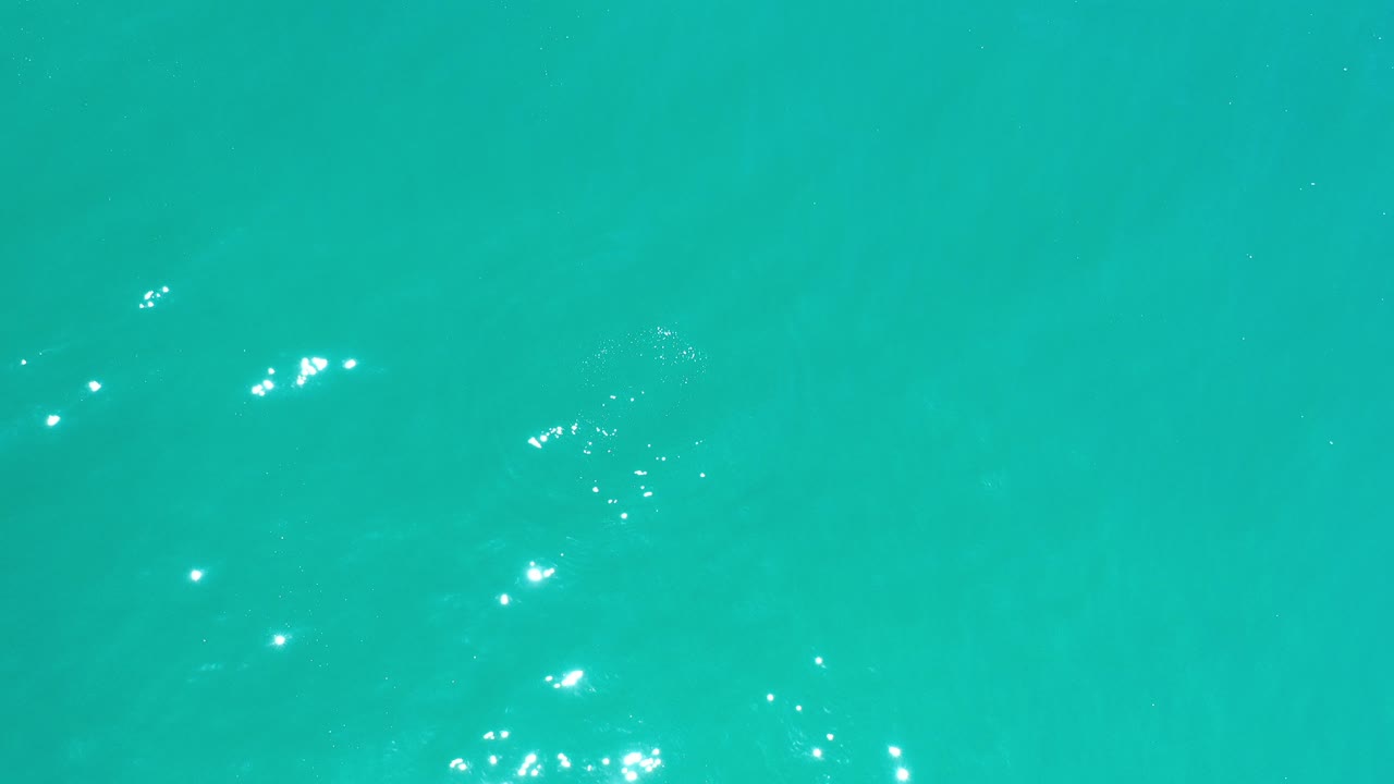 Turquoise ocean water in Los Cabos fills the frame with scattered white sun glints near the surface and no visible people.