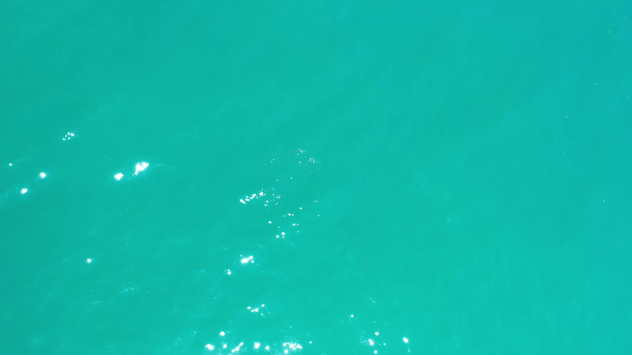 Clear blue-green Los Cabos water shows a wider patch of surface sparkle across the upper part of the frame, with no visible people.
