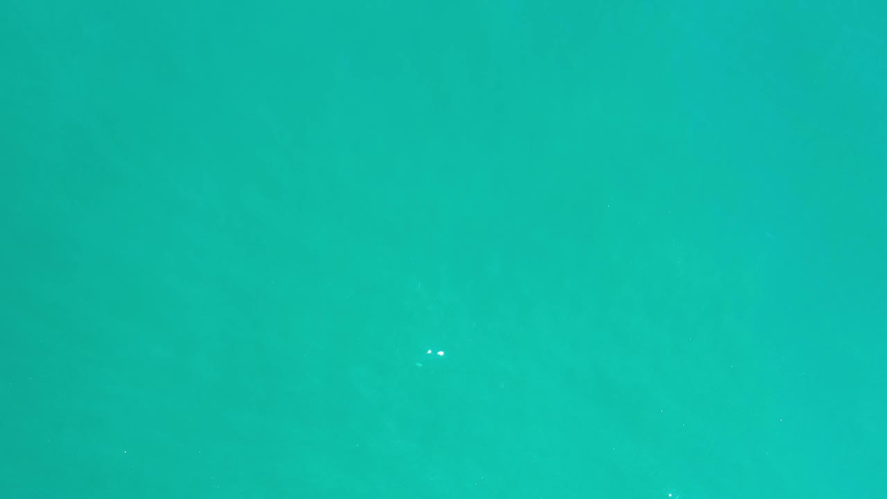 Aerial view of teal sea in Los Cabos, Mexico, with faint green patches below the surface and no visible people.