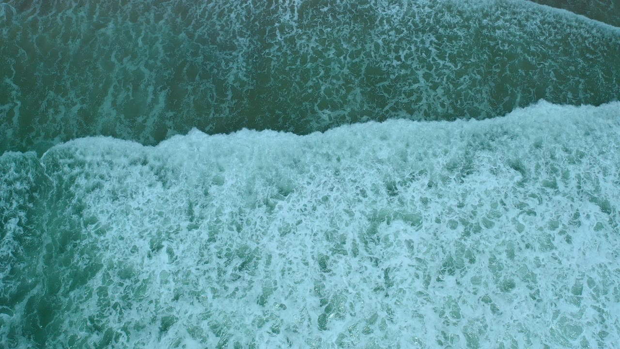 Overhead view of white surf spreading across teal water in Los Cabos, Mexico, with no visible people.