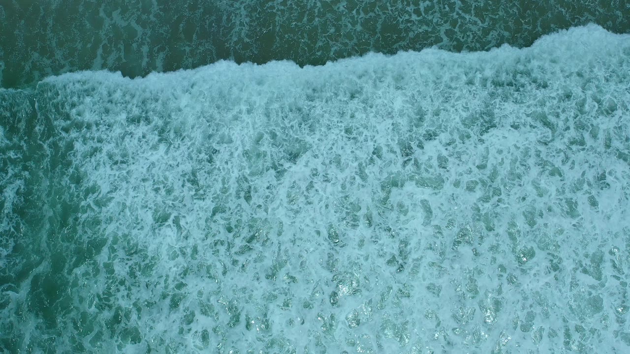 Dense white surf fills most of the overhead shoreline view.