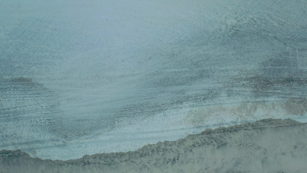 Overhead Los Cabos shoreline frame with foamy water bands across the upper beach and no visible people.