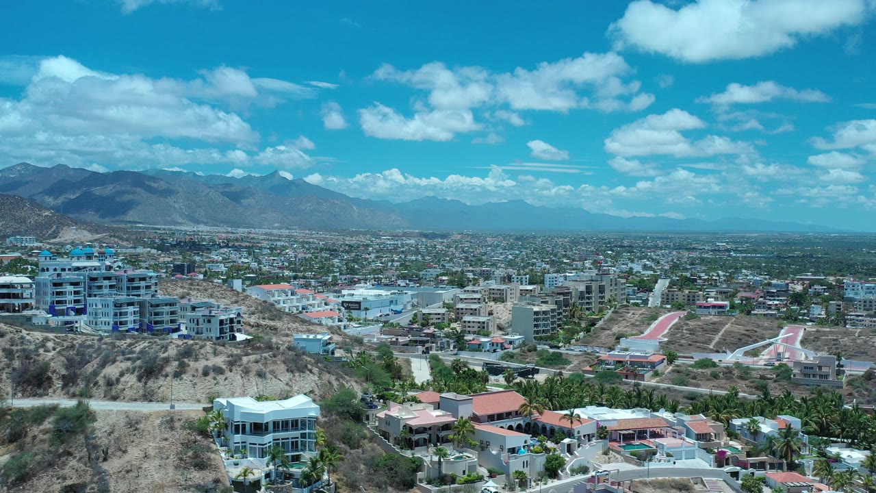 Wide aerial view of hillside homes, city blocks, mountains, and blue sky.