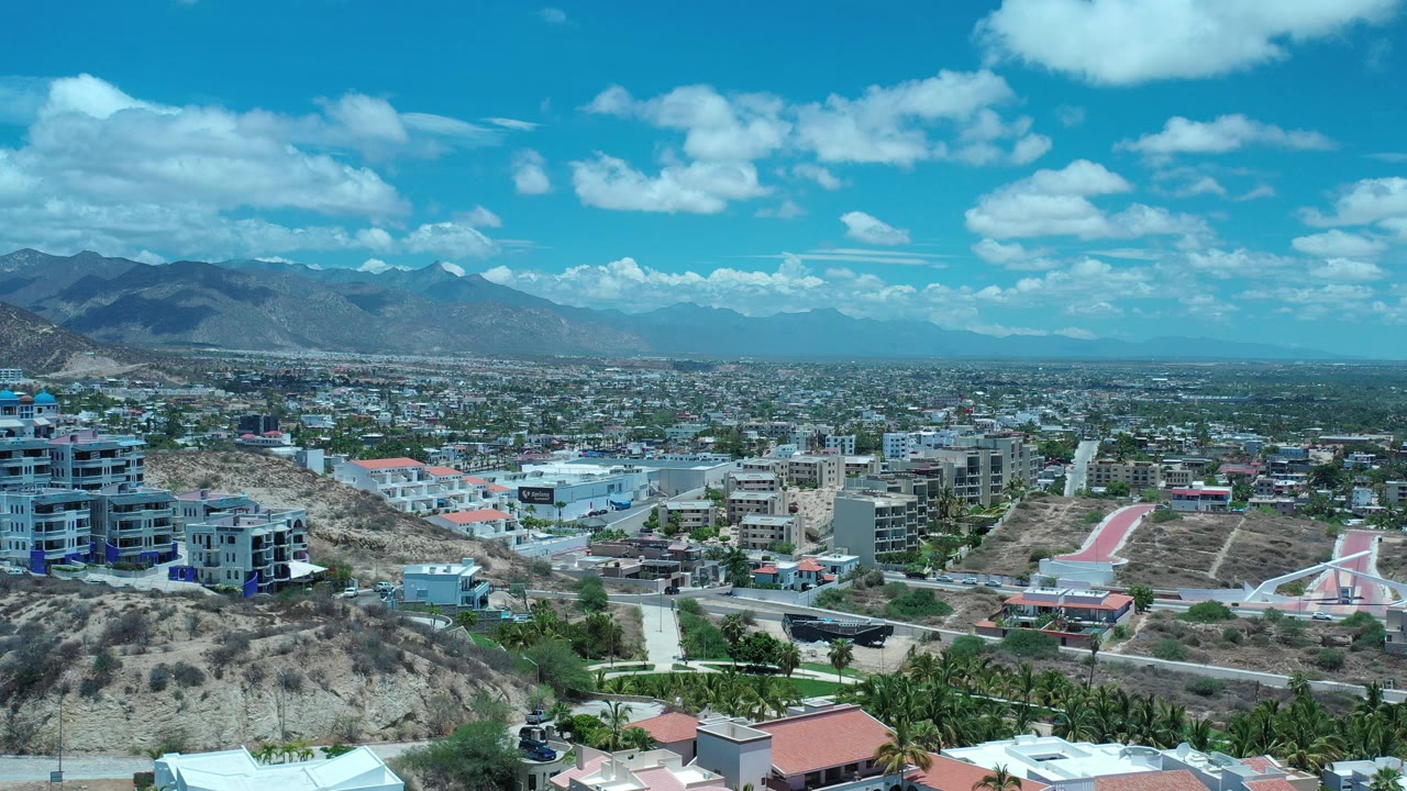 Elevated view of a town below mountains and blue sky.