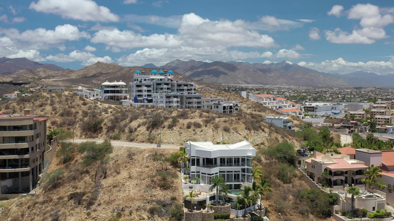 Hillside houses under blue sky with distant mountains.
