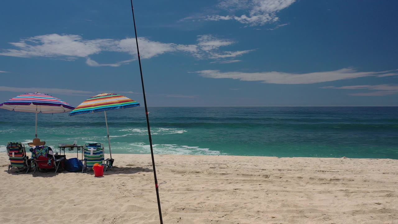 The beach chairs and two colorful umbrellas remain near the lower left of the Los Cabos frame as small waves break across the turquoise water behind them.