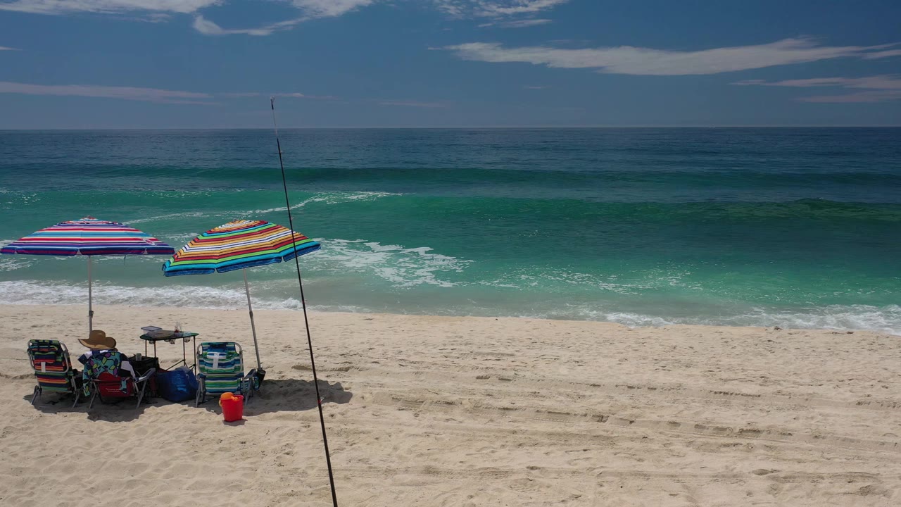 Second frame shows the same Los Cabos umbrella setup slightly centered against darker blue-green water and low white surf, with no visible people.