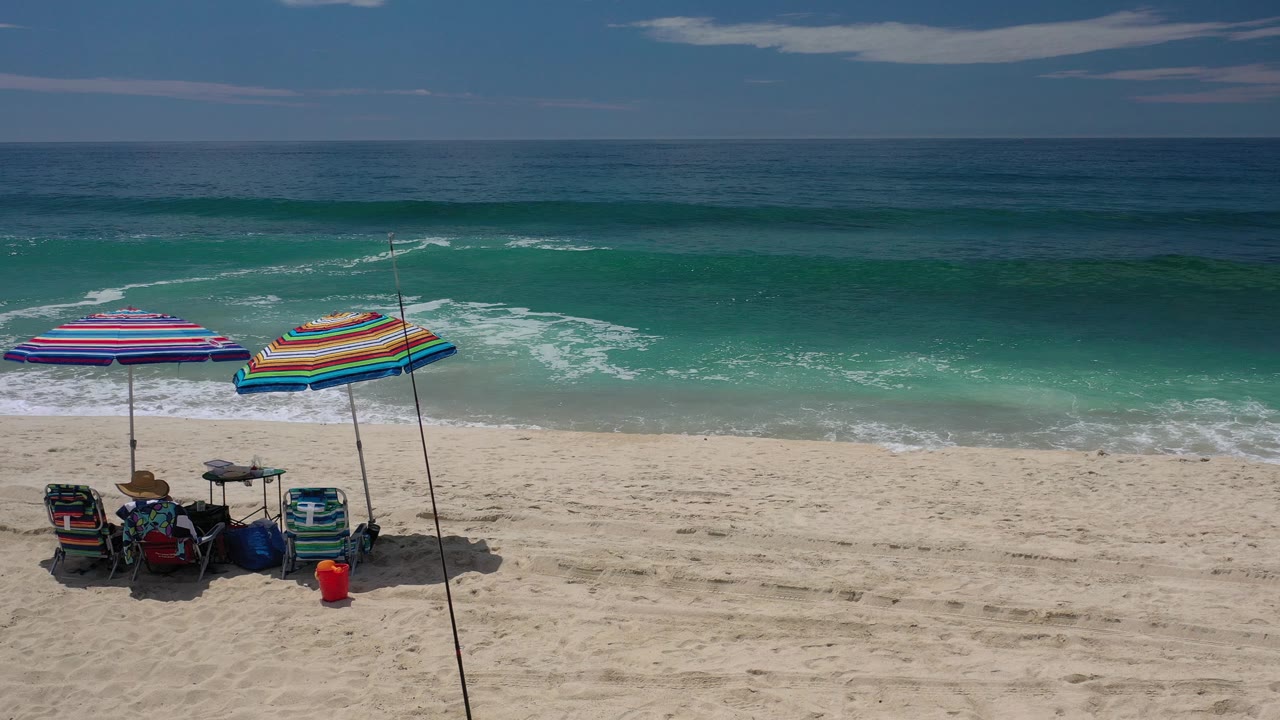 Beach gear under colorful umbrellas facing rolling ocean waves