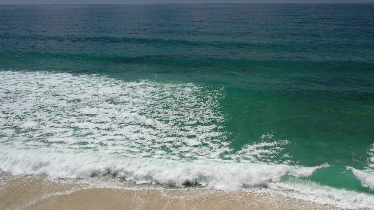 High-angle view of green ocean water and white surf foam in Los Cabos, Mexico, with the horizon across the top and no visible people.