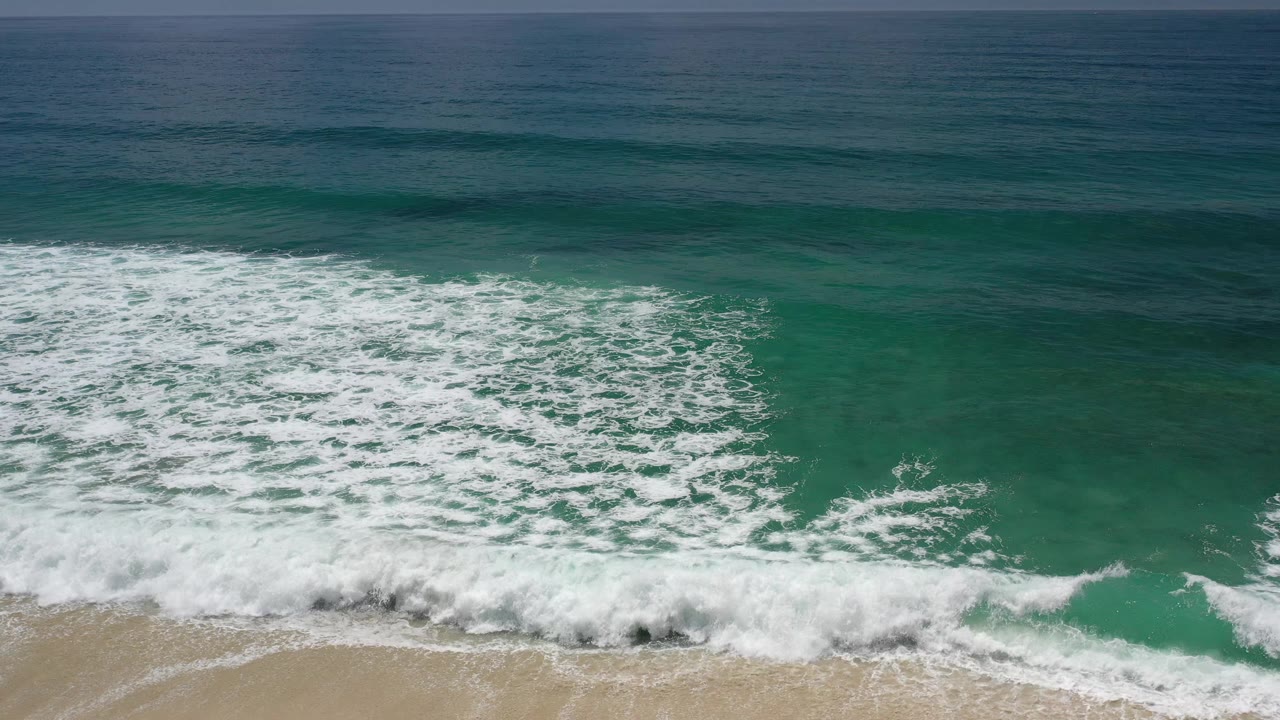 Green sea water in Los Cabos, Mexico, with a larger patch of white foam spreading across the lower half and no visible people.