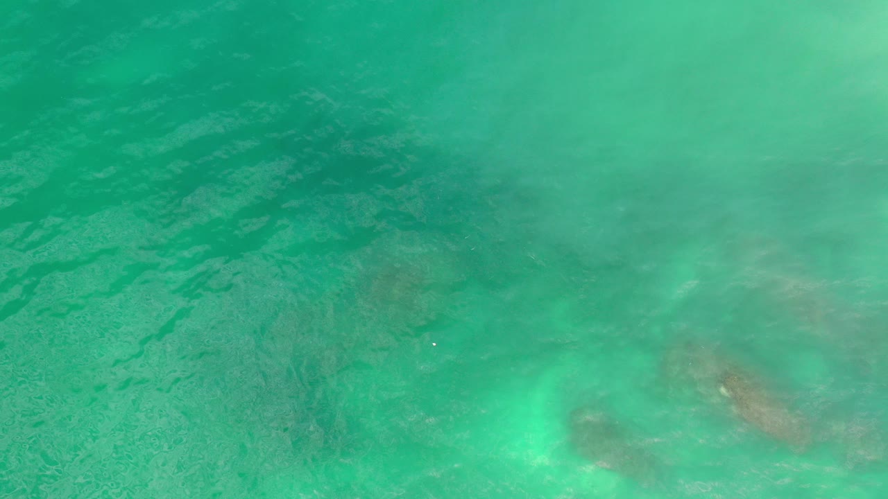 Overhead view of turquoise ocean water near Los Cabos, Mexico, with rippled sunlight, faint submerged patches, and no visible people.