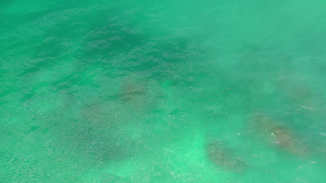 Overhead view of blue-green ocean water in Los Cabos, Mexico, with pale ripples and faint darker shapes below the surface, no visible people.