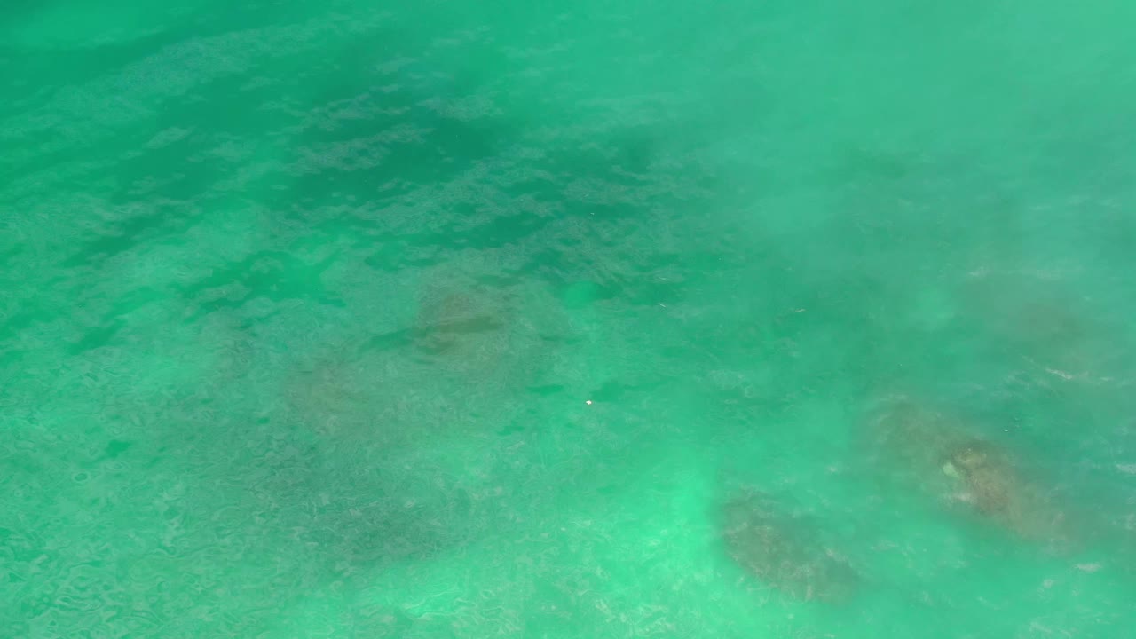 Blue-green water fills the Los Cabos frame with a darker submerged patch near the lower center and a brighter shallow area at the lower left, no visible people.