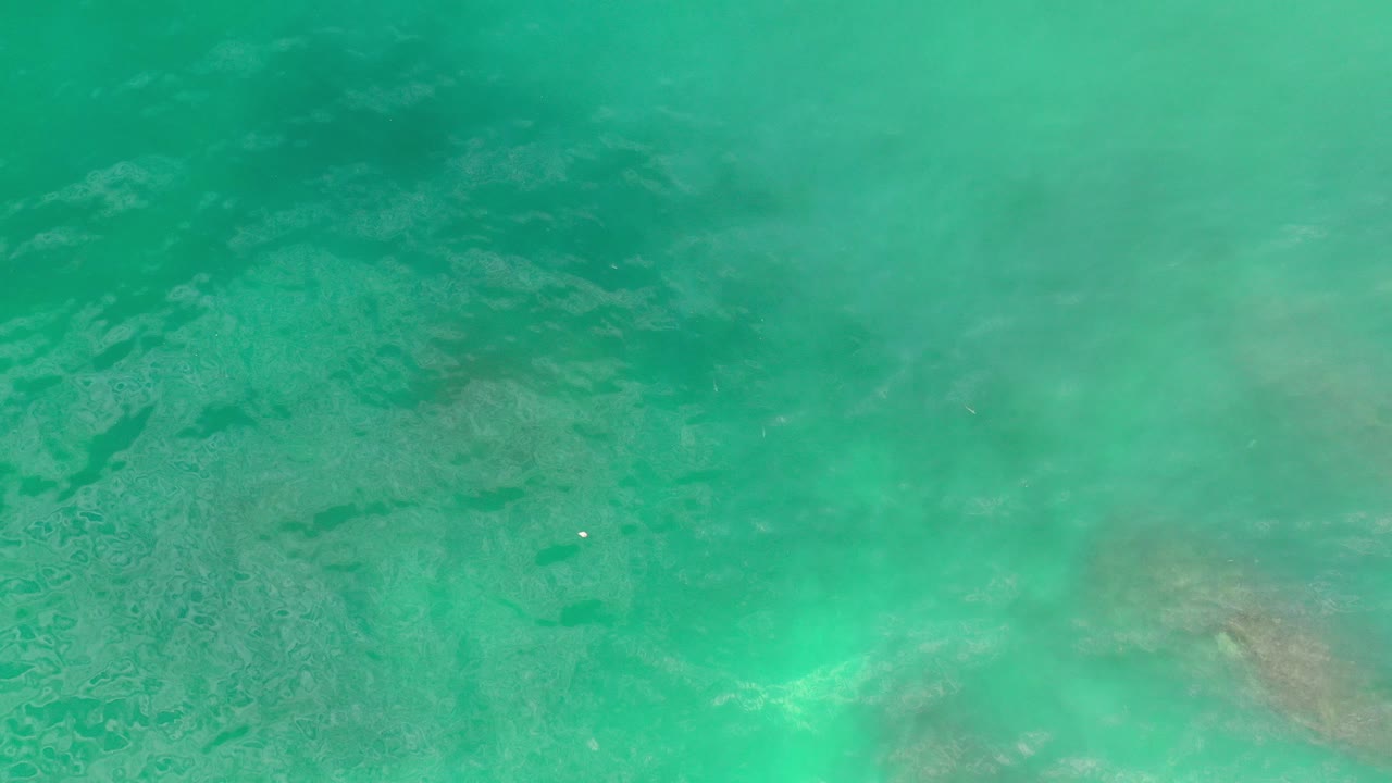 Turquoise water in Los Cabos fills the frame with faint submerged sand or rock patches and no visible people.