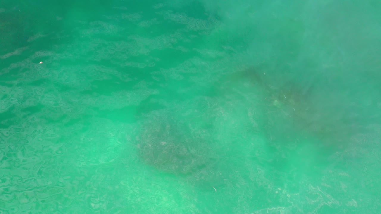 Overhead view of turquoise water in Los Cabos, Mexico, with faint submerged dark patches and no visible people.