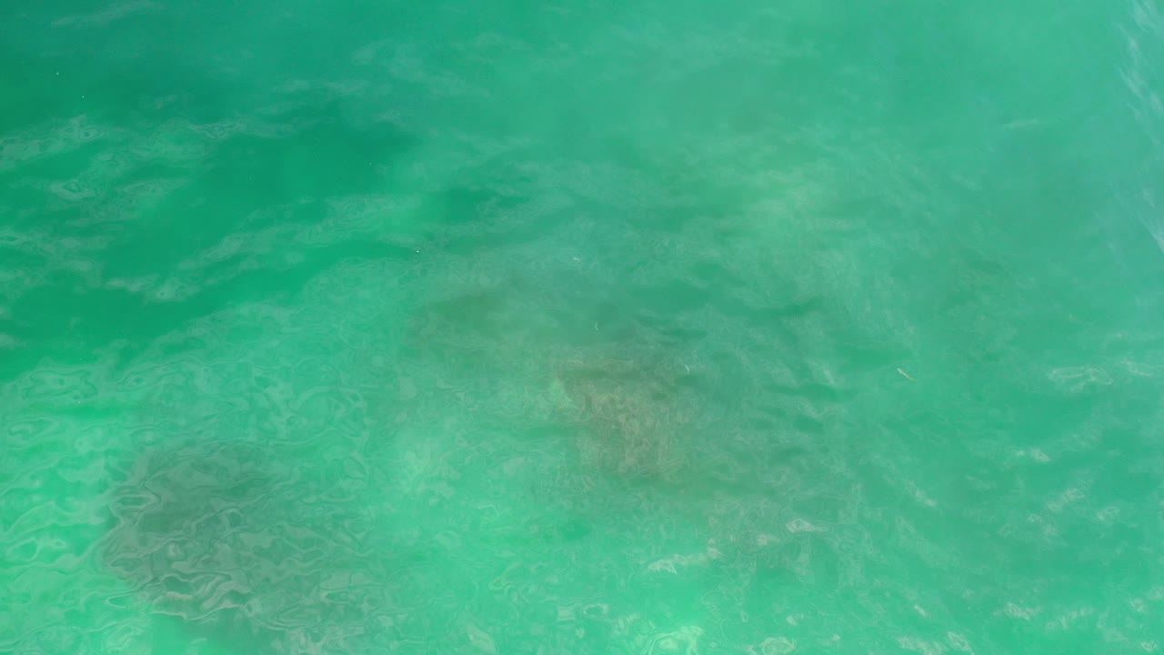 Overhead view of green turquoise seawater in Los Cabos, Mexico, with faint darker reef patches below the surface and no visible people.