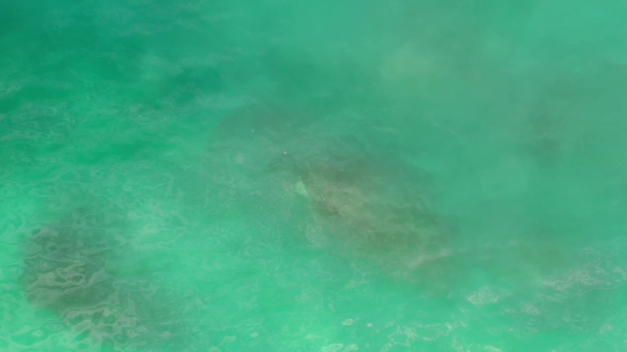 Overhead Los Cabos ocean frame with clear green-blue water, faint darker rock forms under the surface, and no visible people or vessels.
