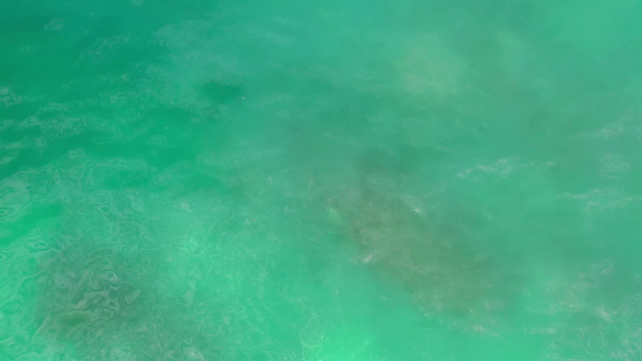 Turquoise ocean water fills the frame in Los Cabos, Mexico, with faint submerged rock shapes and soft surface shimmer, no visible people.