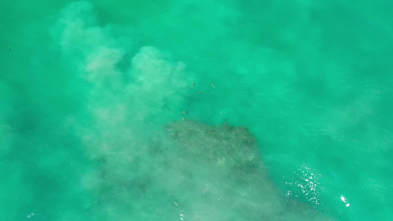 Overhead Los Cabos sea water shows the pale wash spreading across the upper frame while the darker underwater patch sits low in frame, with no visible people.