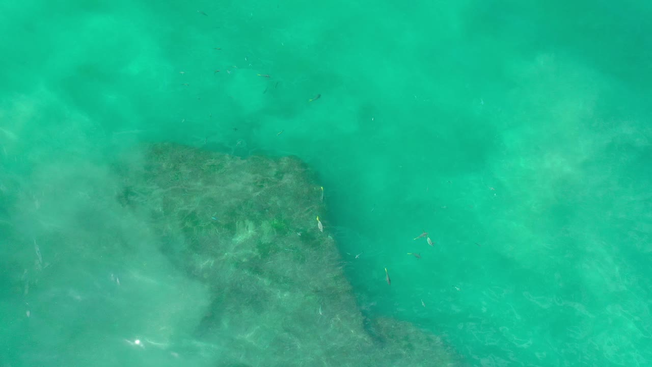 Aerial turquoise water with a broad darker reef shape below.