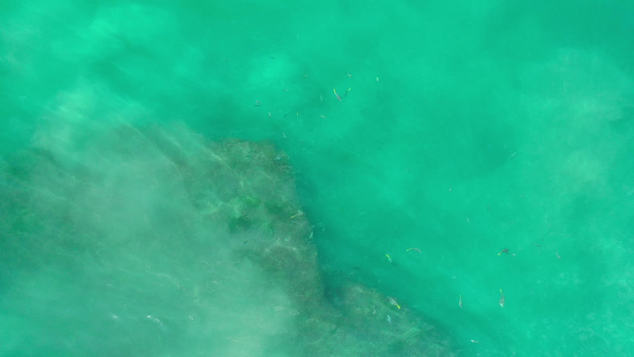 Overhead view of turquoise ocean water in Los Cabos, Mexico, with a darker submerged patch entering from the lower left and no visible people.