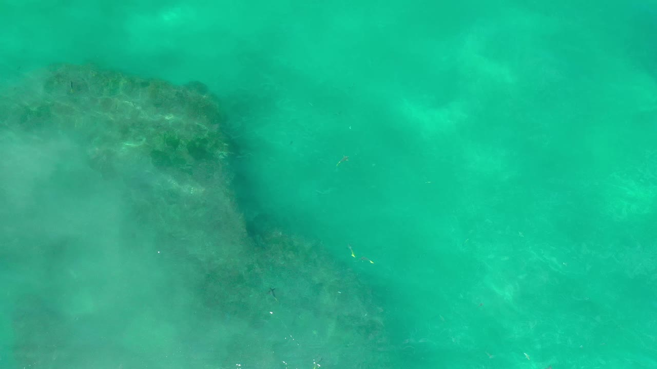 Overhead Los Cabos water view with the darker submerged formation closer to center, cloudy pale water on the left, and no visible people.