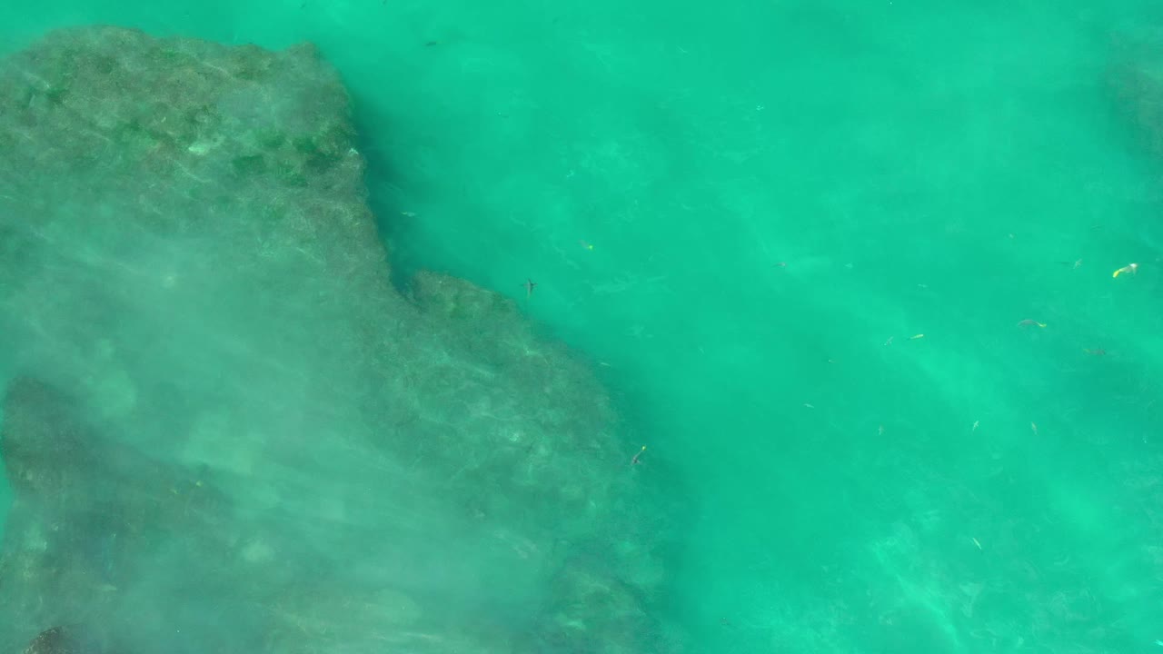 Clear green water blurs the edge of a large underwater rock in Los Cabos, Mexico, while pale ripples pass across the surface with no visible people.