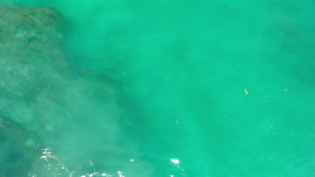 Bright turquoise water with faint submerged shapes and sun glints.