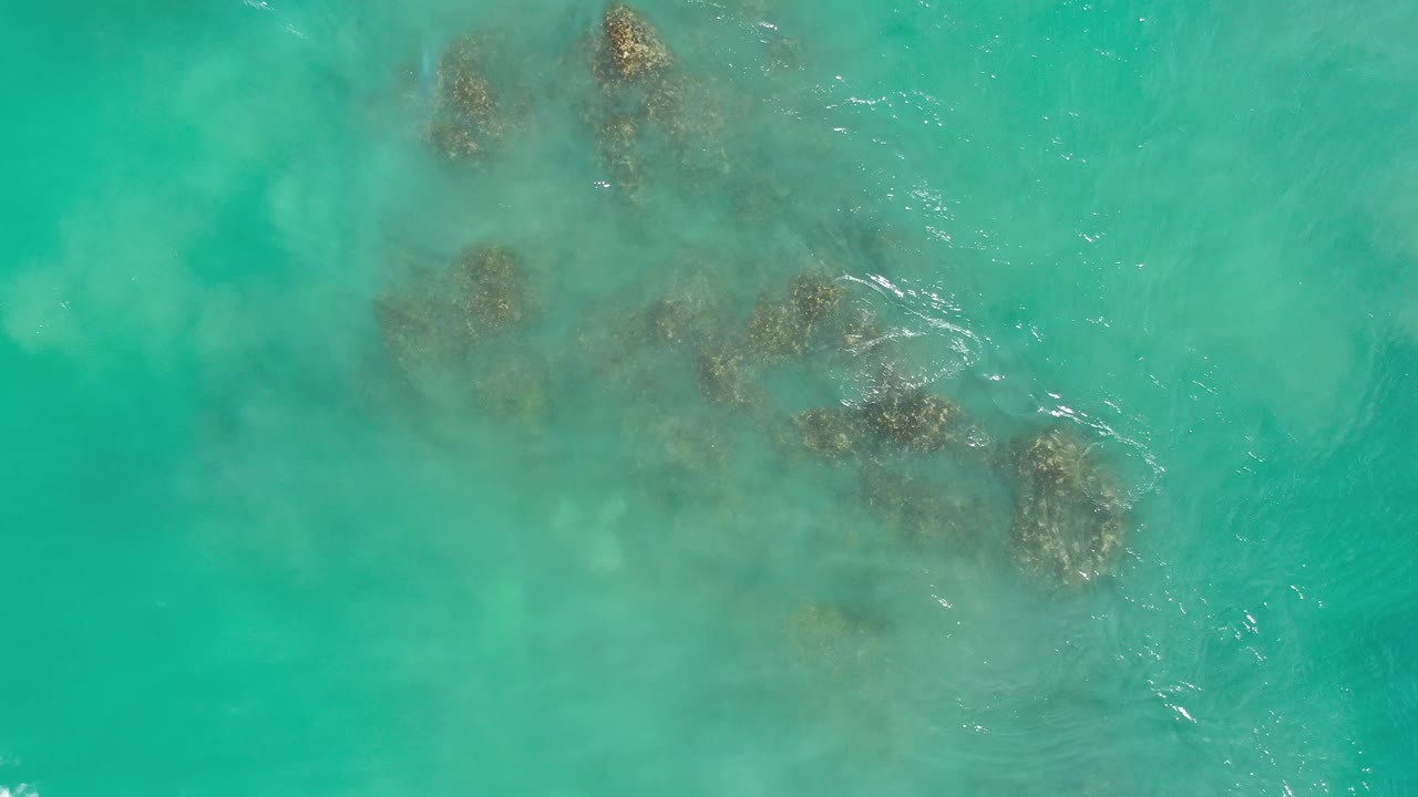 Turquoise water with clustered rocks and faint wave streaks