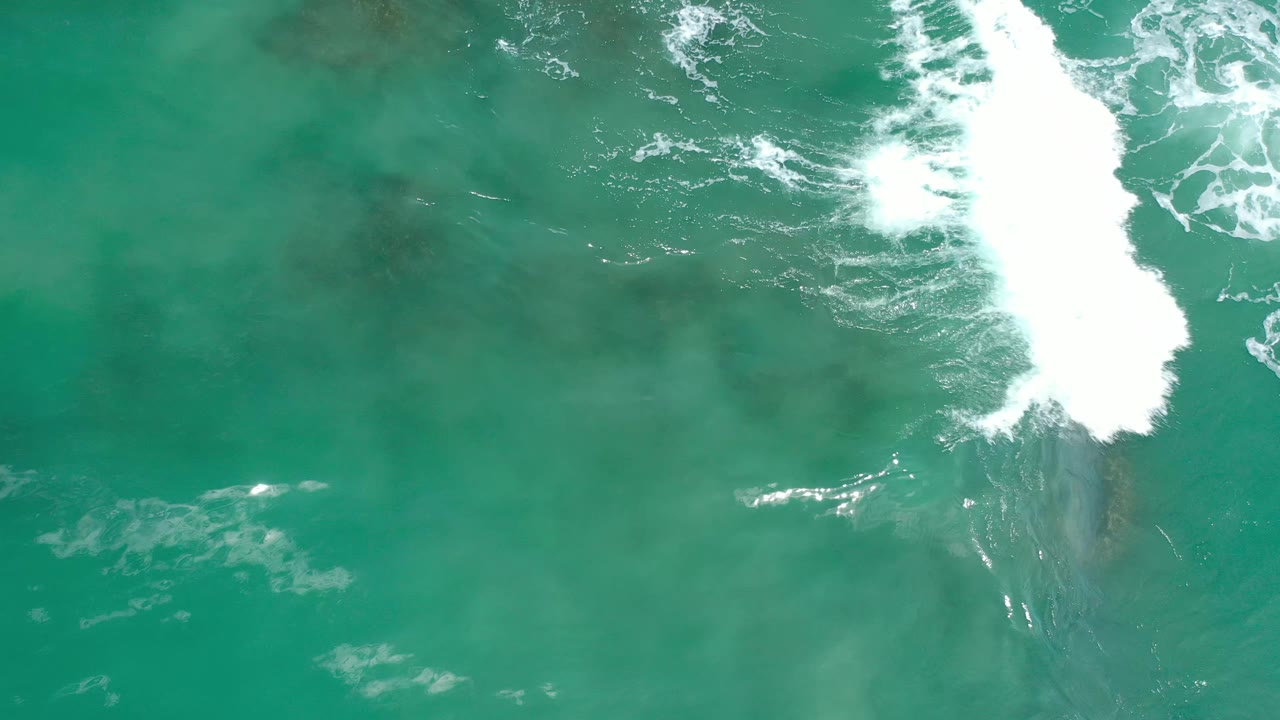 Turquoise coastal water fills the frame in Los Cabos, Mexico, with white foam near the upper center and darker reef texture visible below, no visible people.