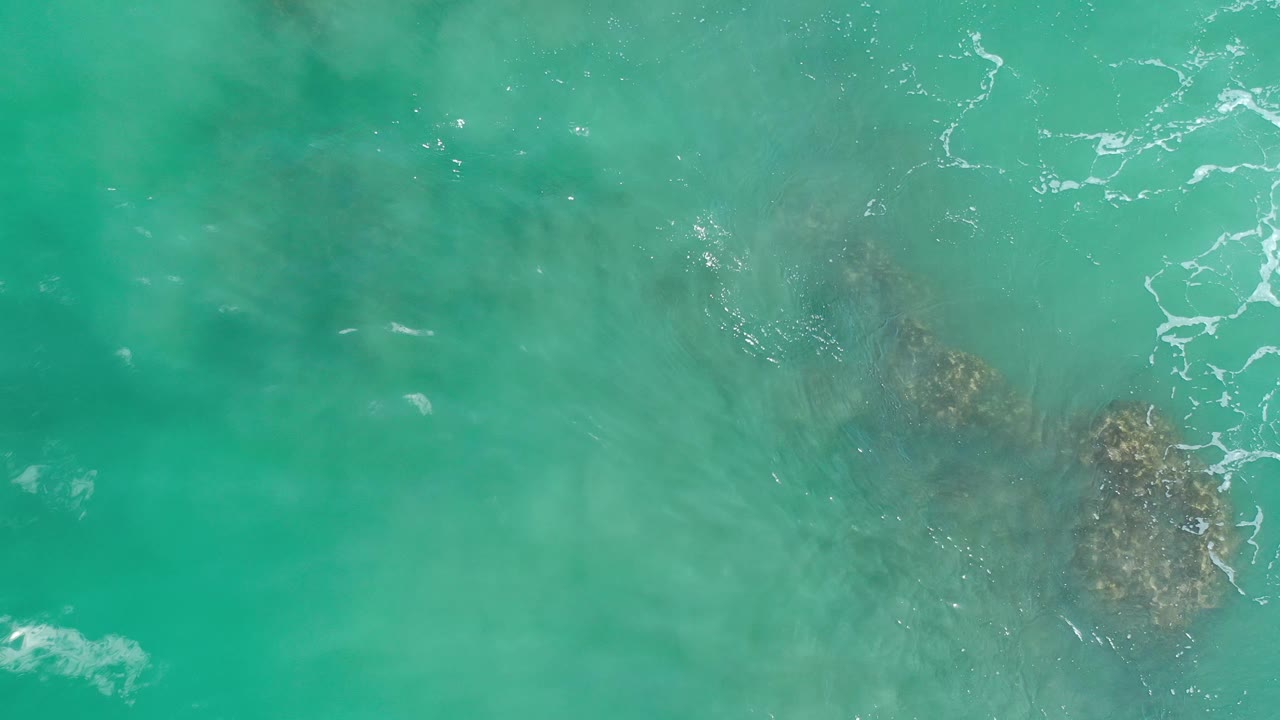 Aerial view of turquoise water and a dark patch below the surface.