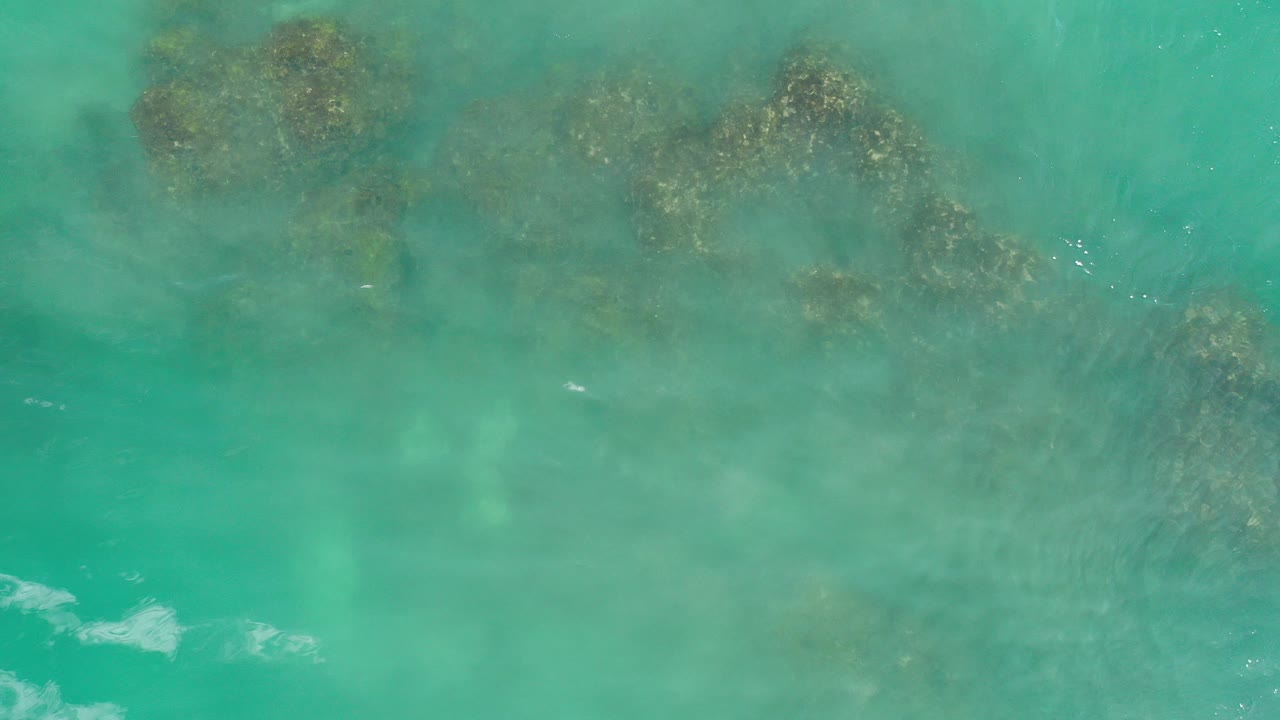 Overhead view of aquamarine water covering dark submerged rocks in Los Cabos, Mexico, with no visible people.