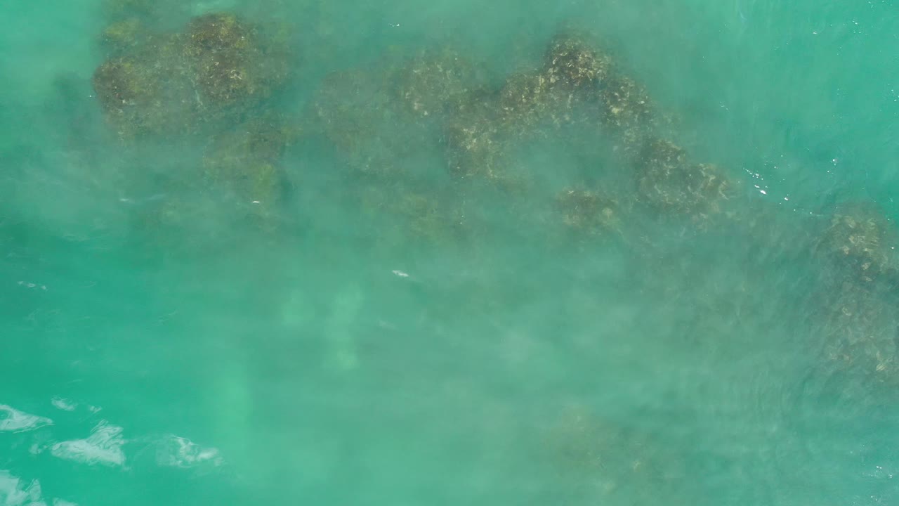 Submerged rock clusters sit beneath pale turquoise water in Los Cabos, Mexico, with faint surface ripples and no visible people.