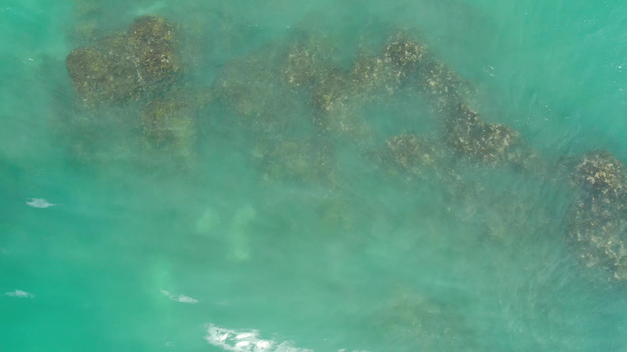 Foam flecks pass over submerged rocks in green-blue water.