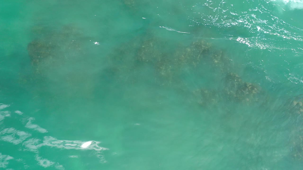 Rocky shallows visible beneath turquoise water with light foam at the edges.