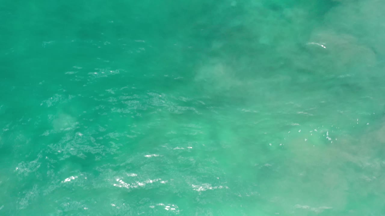 Green water fills the Los Cabos frame with faint pale patches below the surface, brighter highlights near the lower edge, and no visible people.