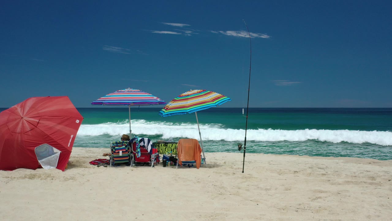 Beach umbrellas, chairs, seated people, sand, and ocean waves.