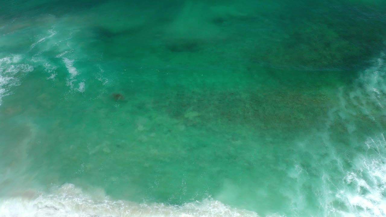 Overhead view of aqua green waves in Los Cabos, Mexico, with white foam entering along the lower edge and no visible people.